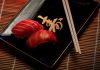 A close-up of two pieces of salmon sushi on a decorative plate with chopsticks.