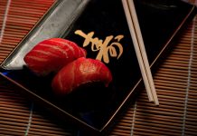 A close-up of two pieces of salmon sushi on a decorative plate with chopsticks.