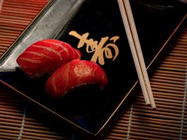 A close-up of two pieces of salmon sushi on a decorative plate with chopsticks.