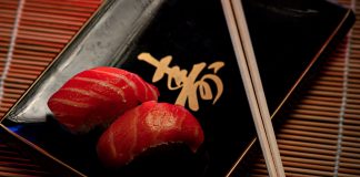 A close-up of two pieces of salmon sushi on a decorative plate with chopsticks.