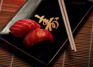 A close-up of two pieces of salmon sushi on a decorative plate with chopsticks.