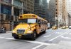 A yellow school bus navigates a busy New York City street amidst tall buildings and taxis.