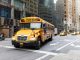 A yellow school bus navigates a busy New York City street amidst tall buildings and taxis.