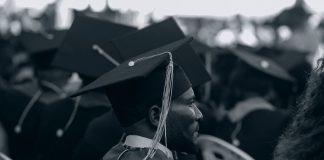 Black and white photo of graduates in caps and gowns at a ceremony.