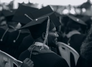 Black and white photo of graduates in caps and gowns at a ceremony.