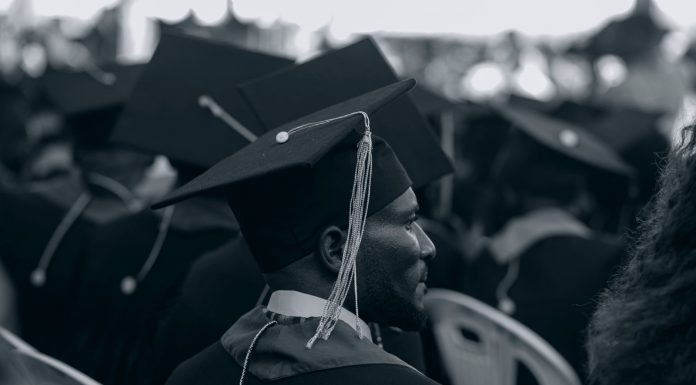 Black and white photo of graduates in caps and gowns at a ceremony.