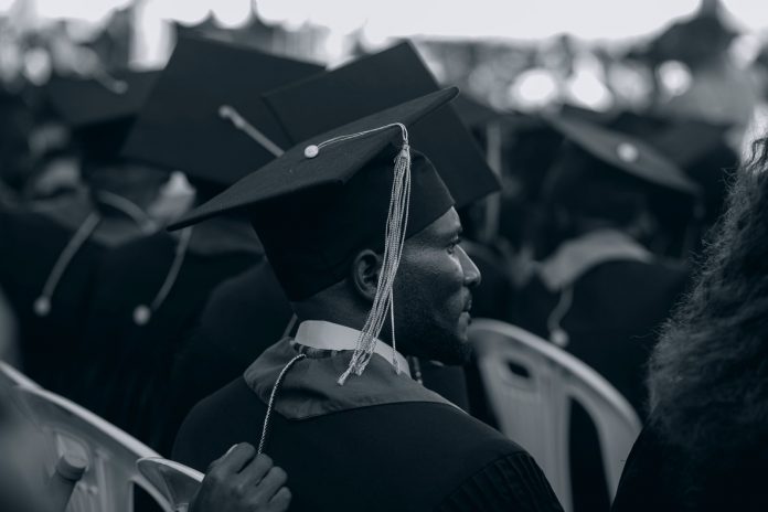 Black and white photo of graduates in caps and gowns at a ceremony.