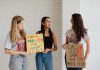 Four Moms, One Mission: New School Board Slate Rises in Jersey City Three women holding advocacy signs supporting women's rights, indoors.