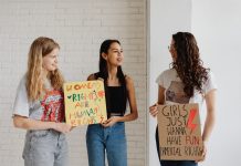 Four Moms, One Mission: New School Board Slate Rises in Jersey City Three women holding advocacy signs supporting women's rights, indoors.