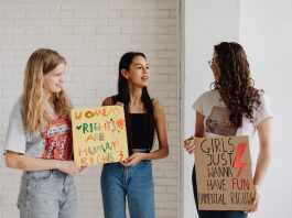Four Moms, One Mission: New School Board Slate Rises in Jersey City Three women holding advocacy signs supporting women's rights, indoors.