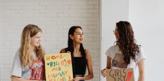 Four Moms, One Mission: New School Board Slate Rises in Jersey City Three women holding advocacy signs supporting women's rights, indoors.