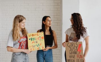 Four Moms, One Mission: New School Board Slate Rises in Jersey City Three women holding advocacy signs supporting women's rights, indoors.