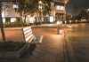 A serene city street scene featuring an empty bench at night, illuminated by streetlights.