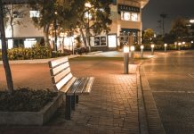 A serene city street scene featuring an empty bench at night, illuminated by streetlights.