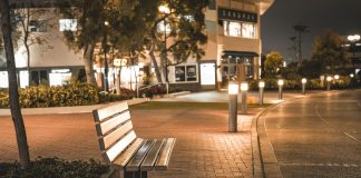A serene city street scene featuring an empty bench at night, illuminated by streetlights.