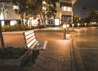 A serene city street scene featuring an empty bench at night, illuminated by streetlights.