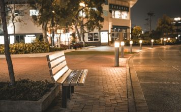 A serene city street scene featuring an empty bench at night, illuminated by streetlights.