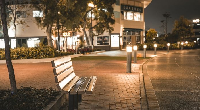 A serene city street scene featuring an empty bench at night, illuminated by streetlights.