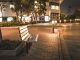 A serene city street scene featuring an empty bench at night, illuminated by streetlights.