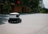 A sleek autonomous food delivery robot navigates a sunny urban landscape, showcasing modern innovation.