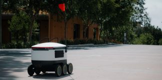 A sleek autonomous food delivery robot navigates a sunny urban landscape, showcasing modern innovation.