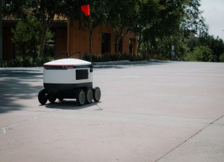 A sleek autonomous food delivery robot navigates a sunny urban landscape, showcasing modern innovation.