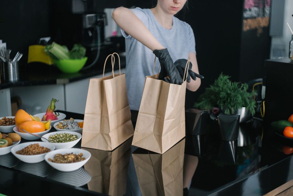A person in a kitchen packing food ingredients into paper bags for takeout orders.