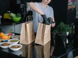 A person in a kitchen packing food ingredients into paper bags for takeout orders.