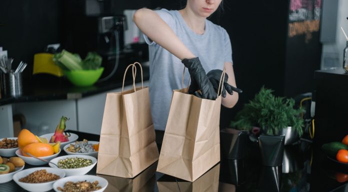 A person in a kitchen packing food ingredients into paper bags for takeout orders.