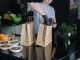 A person in a kitchen packing food ingredients into paper bags for takeout orders.