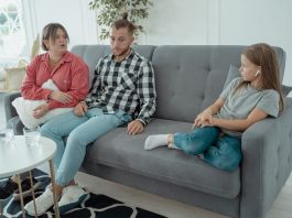 A family sits together on a sofa, discussing in a comfortable home setting, indicating a counseling session.