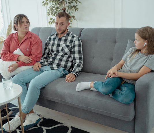 A family sits together on a sofa, discussing in a comfortable home setting, indicating a counseling session.
