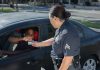A police officer hands a ticket to a driver in a car on a sunny day street.