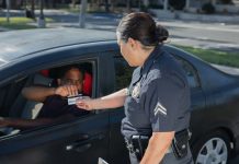 A police officer hands a ticket to a driver in a car on a sunny day street.