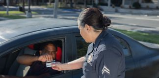 How to Get a Driver’s License in NJ: Newark Guide (2026) A police officer hands a ticket to a driver in a car on a sunny day street.