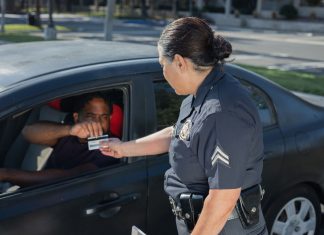 A police officer hands a ticket to a driver in a car on a sunny day street.