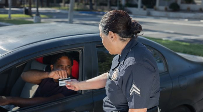 A police officer hands a ticket to a driver in a car on a sunny day street.