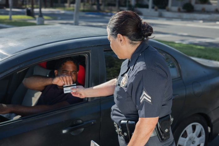 how-to-get-drivers-license-nj-newark-guide-2026 A police officer hands a ticket to a driver in a car on a sunny day street.