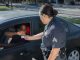 A police officer hands a ticket to a driver in a car on a sunny day street.