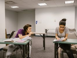 Two college students in a classroom setting, one appears to be copying from the other's paper.
