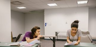 Two college students in a classroom setting, one appears to be copying from the other's paper.