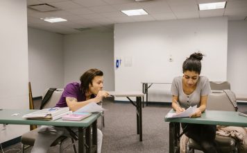 Two college students in a classroom setting, one appears to be copying from the other's paper.
