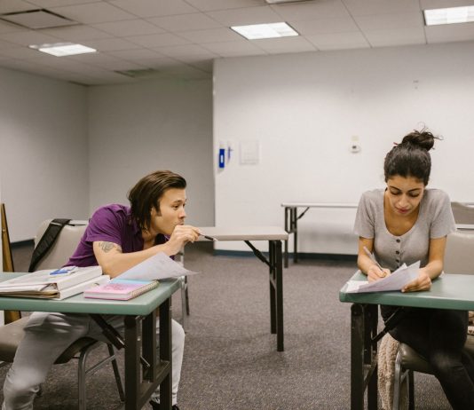 Two college students in a classroom setting, one appears to be copying from the other's paper.