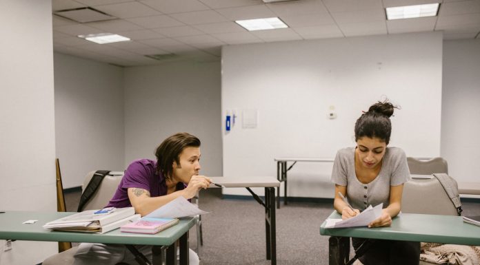 Two college students in a classroom setting, one appears to be copying from the other's paper.