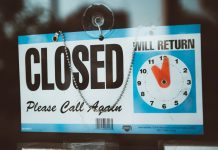 A close-up view of a 'Closed' sign on a door, displaying a return time.