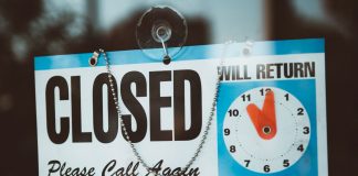 A close-up view of a 'Closed' sign on a door, displaying a return time.