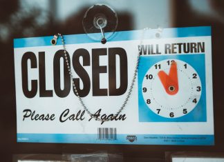 A close-up view of a 'Closed' sign on a door, displaying a return time.