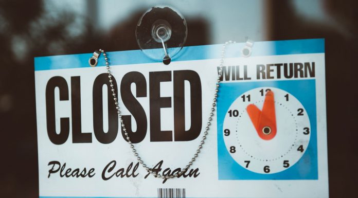 A close-up view of a 'Closed' sign on a door, displaying a return time.