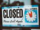 A close-up view of a 'Closed' sign on a door, displaying a return time.