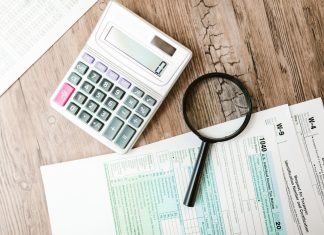 Tax forms laid out with a calculator and magnifying glass on a wooden surface, perfect for finance themes.